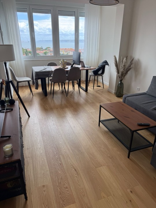 Sala mobilada com soalho de madeira clara e vista para o rio