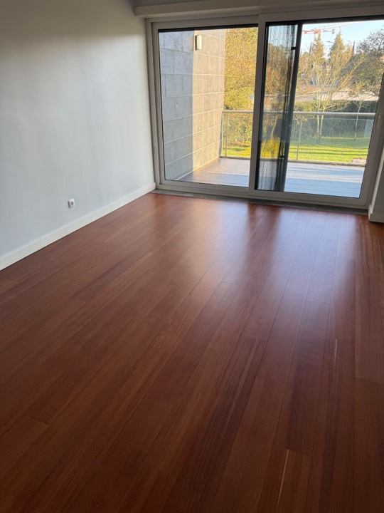 Soalho de madeira em tom avermelhado numa sala com janela para o jardim