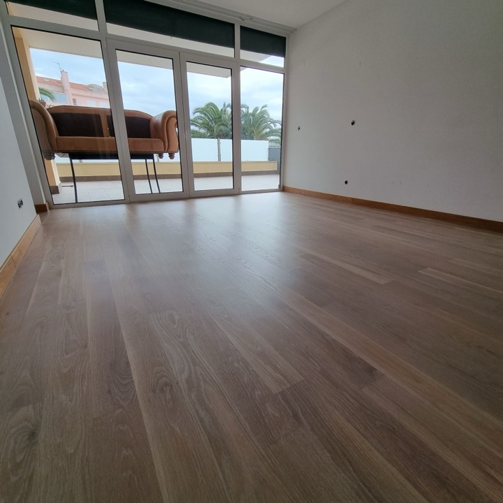 Soalho de madeira clara numa sala com portas para um terraço