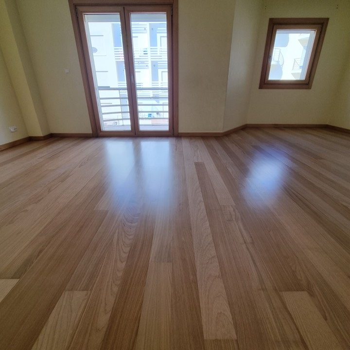 Soalho de madeira clara envernizado numa sala com porta para a varanda