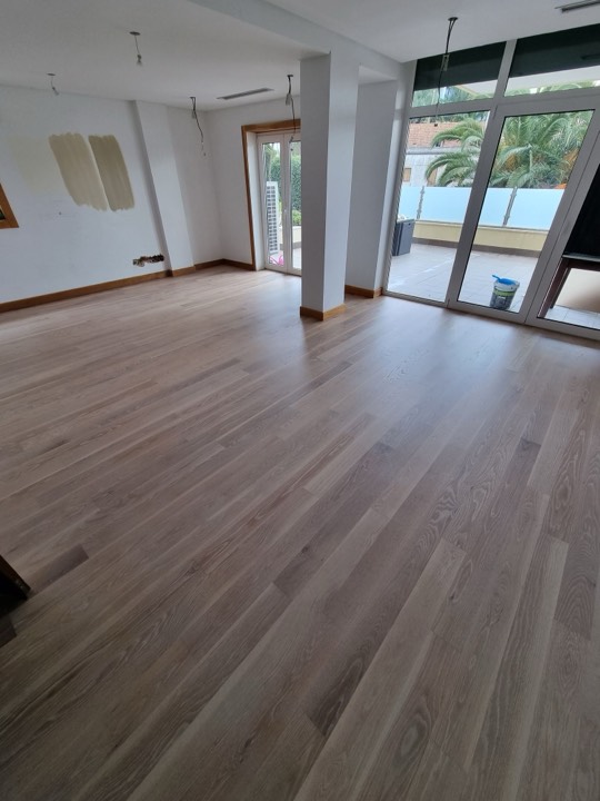 Sala ampla com soalho de madeira clara e portas para o terraço